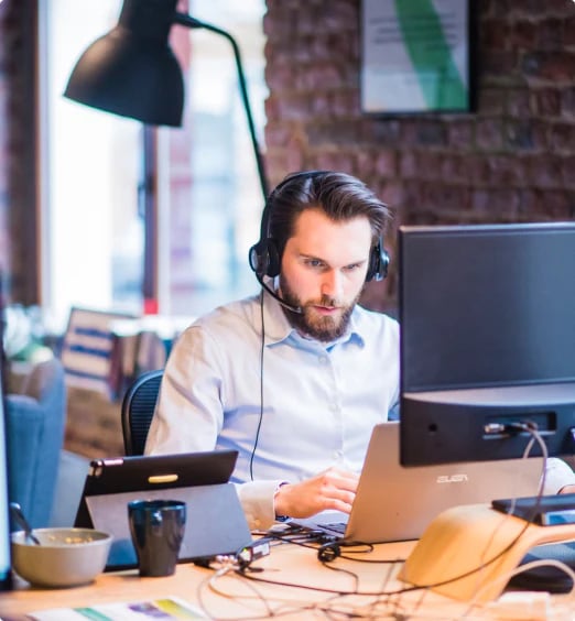 Guy wearing headphones sitting at desk with laptop and tablet