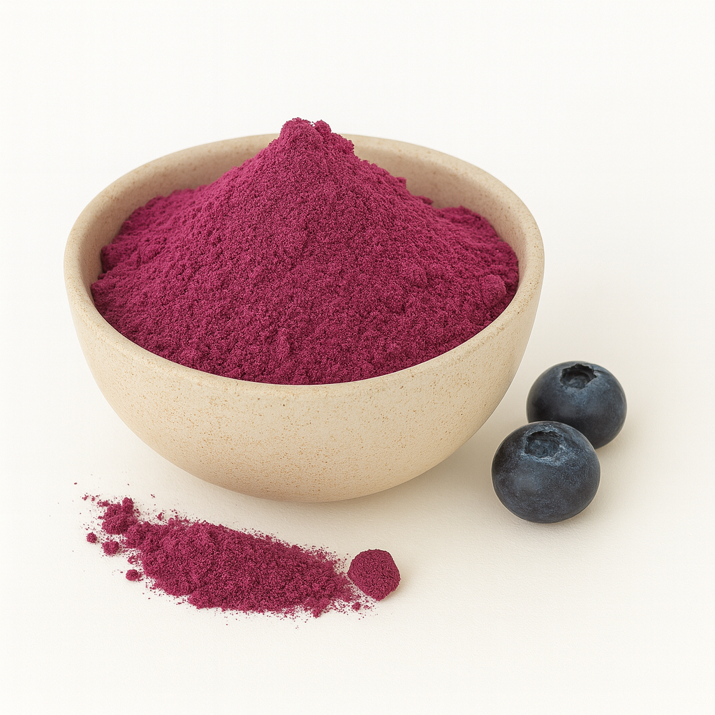 A beige bowl filled with purple blueberry juice powder on a white background, with a small pile of powder and two fresh blueberries beside it.