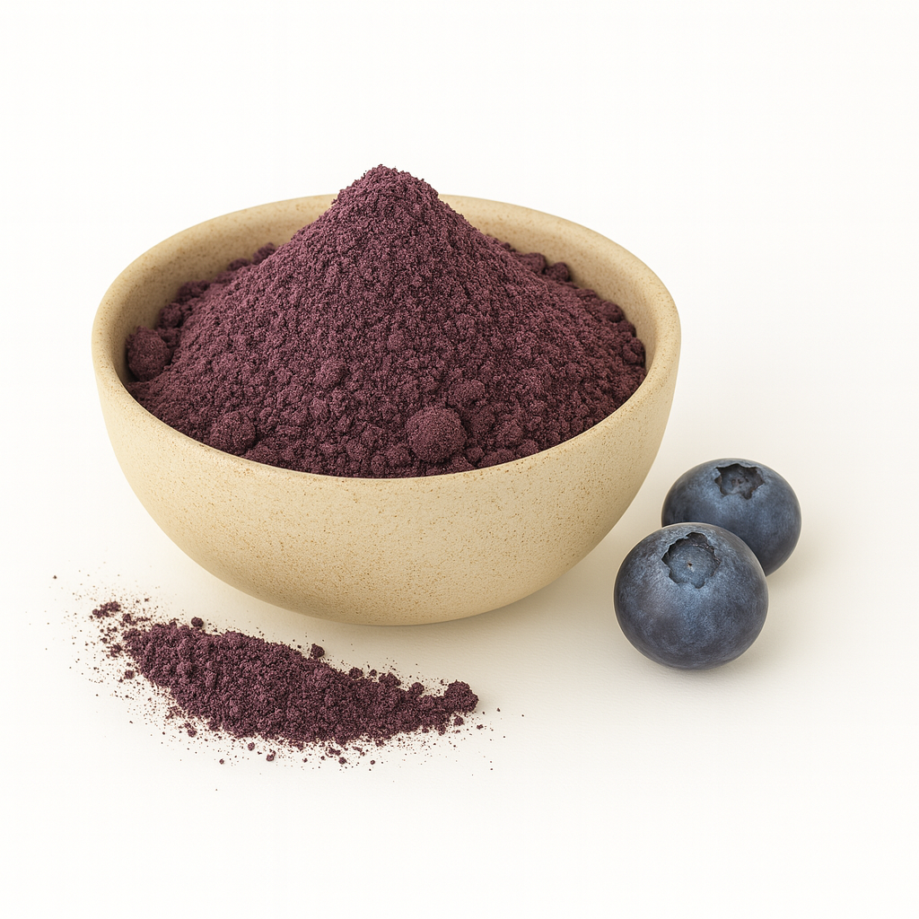 A beige bowl filled with purple blueberry powder on a white background, with a small pile of powder and two fresh blueberries beside it.