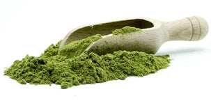 This is a picture of a green superfood powder on a white wooden spoon, with a white background