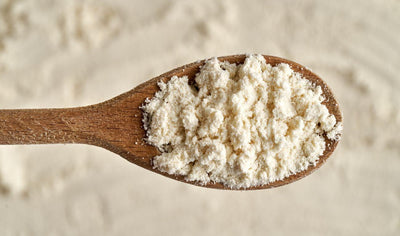 This is a picture of a wooden spoon with whey protein concentrate, on a background of protein powder in a table