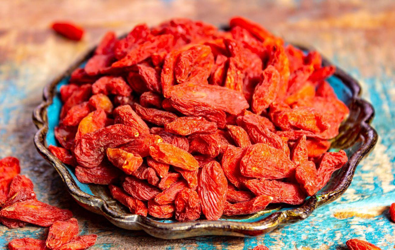 This is an image of bright red Goji Berries in a bowl on a brown table