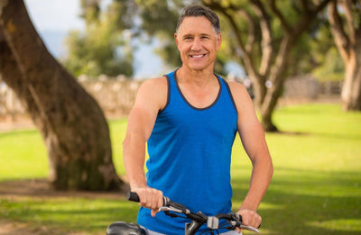 This is an image of a man in a blue tank top with his bicycle in nature with trees in the background
