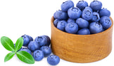 Image of a bunch of fresh Blueberries in a wooden bowl and some outside the bowl and green leaves