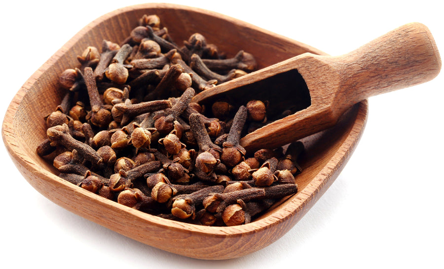 Cloves piled together in a wooden bowl with wooden scoop on white background