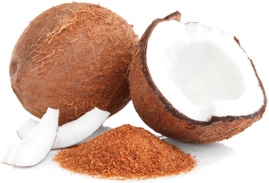 Image of a pile of brown Coconut Palm Sugar next to fresh coconuts one of whom is cracked opened