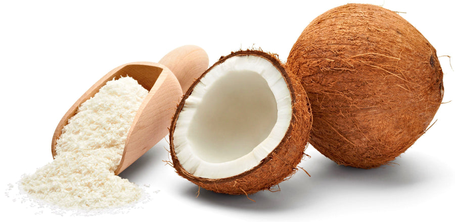 Image of whole, halved Coconut next to a wooden serving spoon containing shredded coconut.