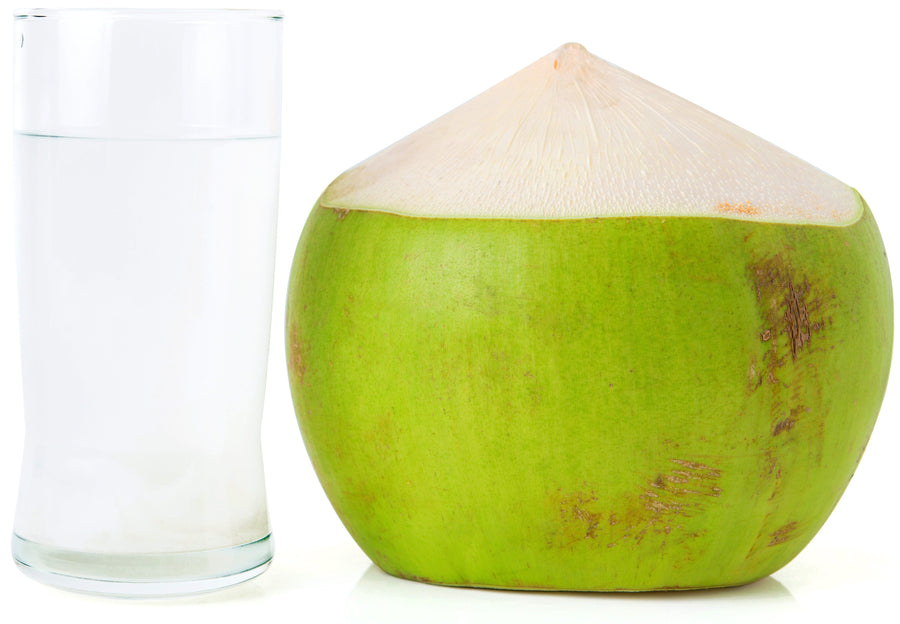 Image of green coconut next to a cup full of coconut water