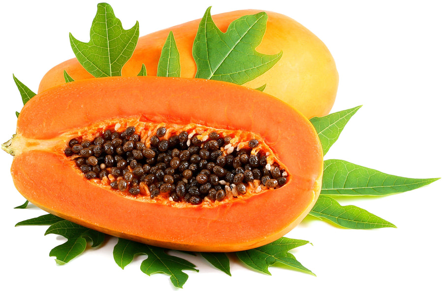 Image of halved Papaya with whole papaya in the background with leaves.
