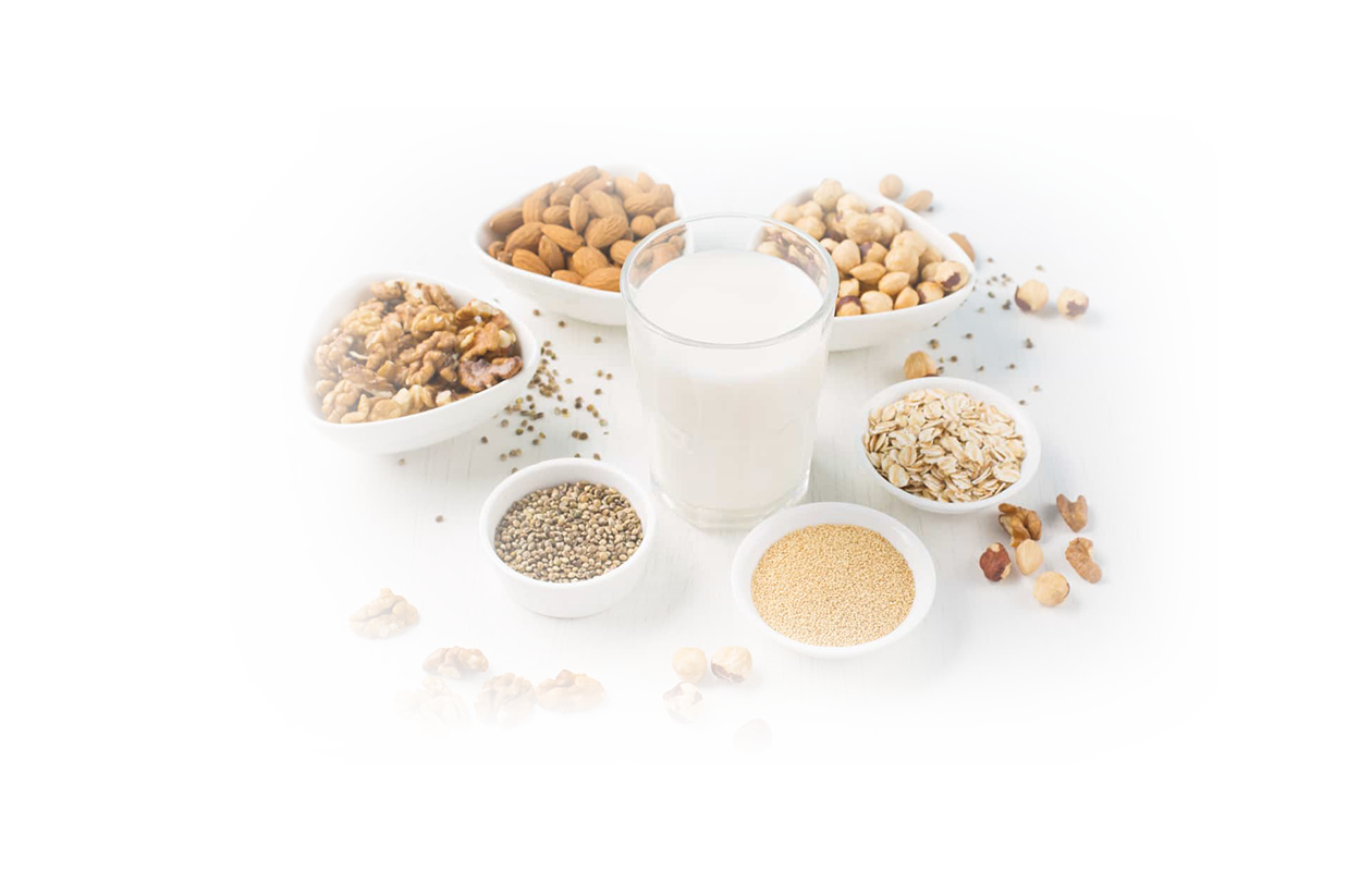 Image of a glass of nut milk surrounded by six bowls of various nuts.