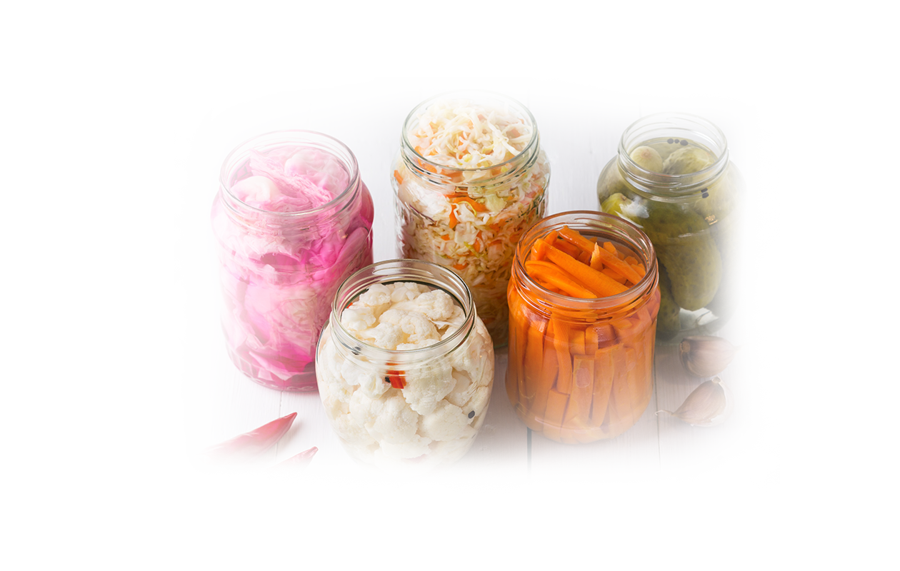 Image of five clear jars on a table containing cauliflower florets, carrot sticks, whole banana peppers, sliced red onions, and shredded cabbage.