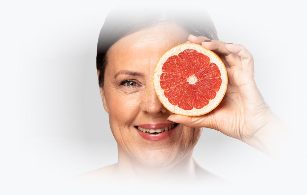 Image of woman holding half a grapefruit slice in front of her face.