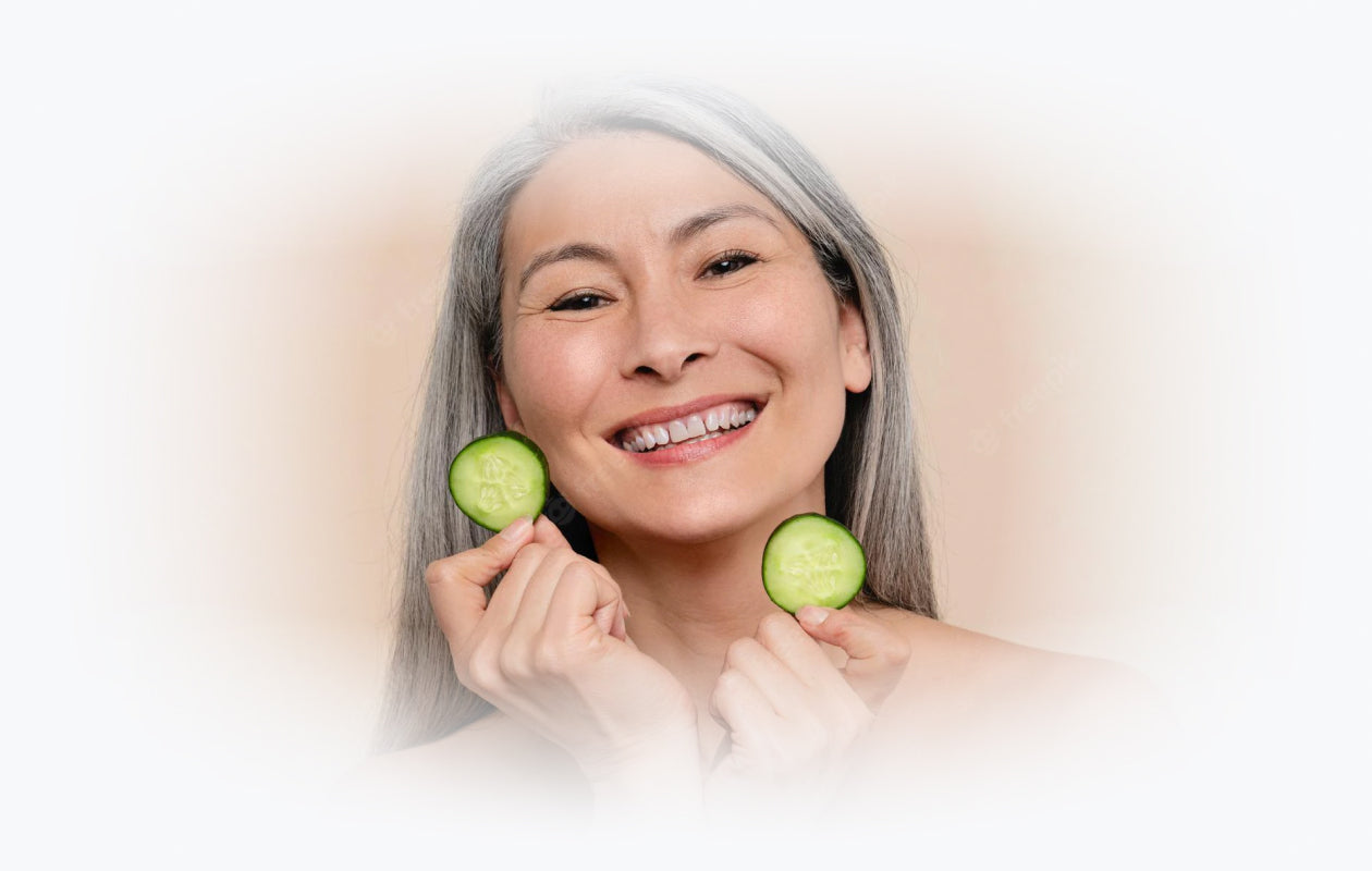 Photo of woman smiling and holding slices of cucumber near her face to depict detoxification