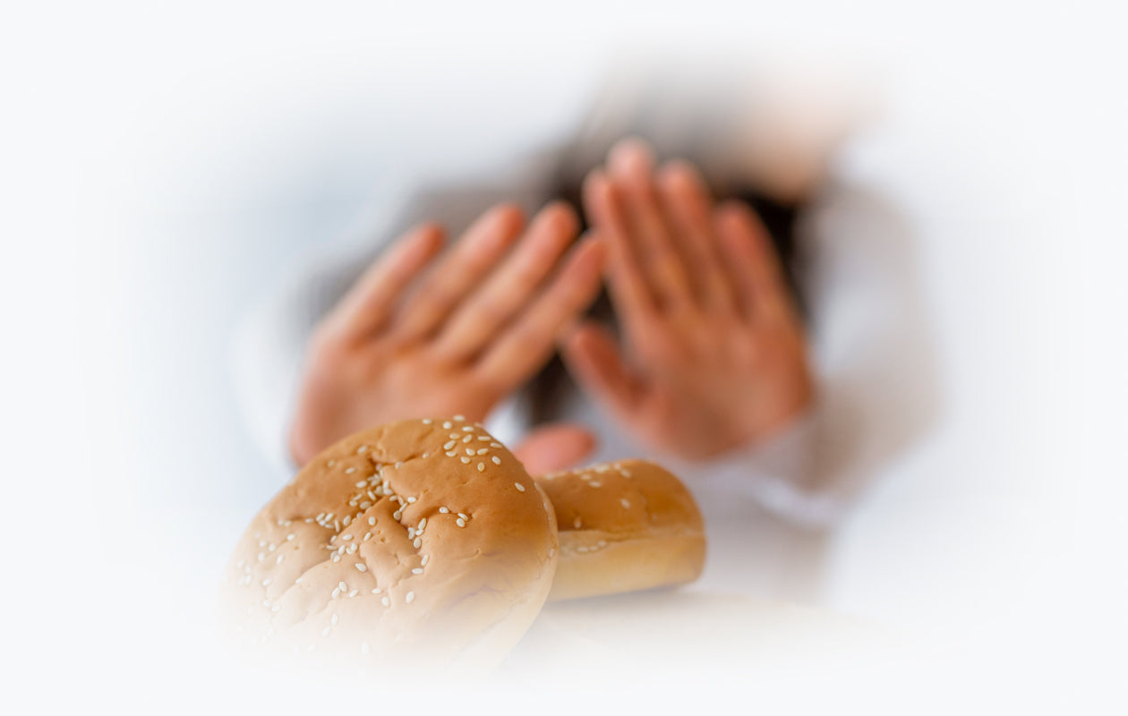Photo of 2 wheat buns and person in background with hands up signifying that do not want it because they are a Celiac