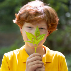 Young boy with red hair holding leaf in front of his face
