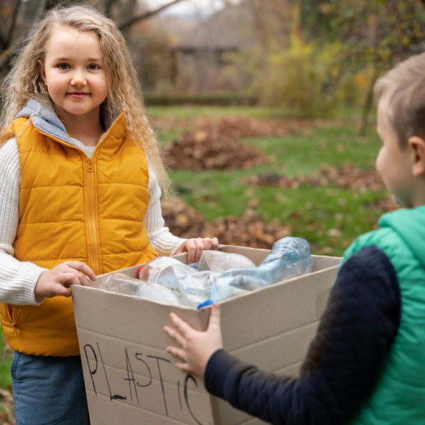 Photo of young girl and boy carrying brown box of recycle plastic