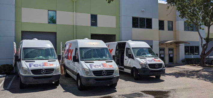 Photo of Three Fedex Express Delivery Vans backed up to ZNF warehouse to pick up packages